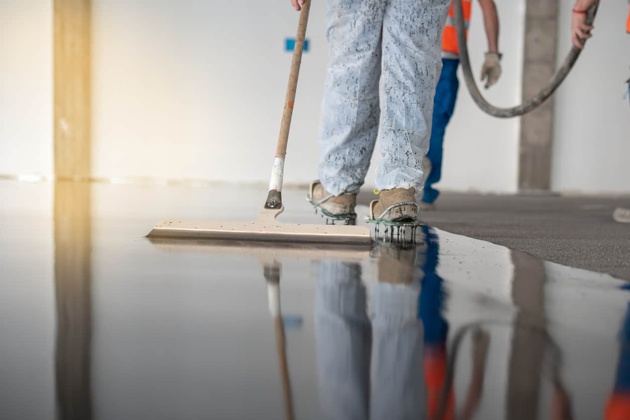Worker working on the floor of an industrial building. Construction worker producing grout and finishing wet concrete floor. Epoxy Flooring